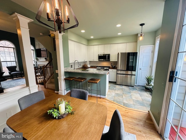 dining space featuring a chandelier, light wood-style flooring, recessed lighting, stairway, and ornate columns