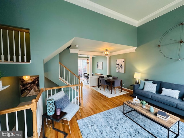 living area featuring a notable chandelier, wood finished floors, baseboards, ornamental molding, and stairway