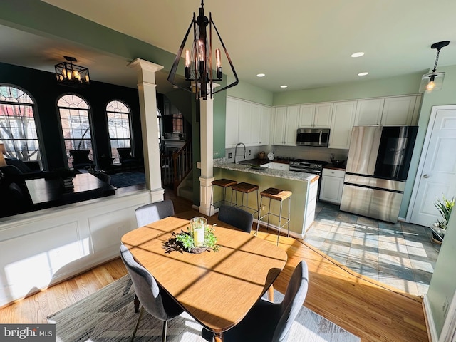 dining area featuring light wood finished floors, stairs, ornate columns, a notable chandelier, and recessed lighting