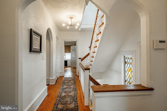 hallway featuring a chandelier, wood-type flooring, and a textured ceiling