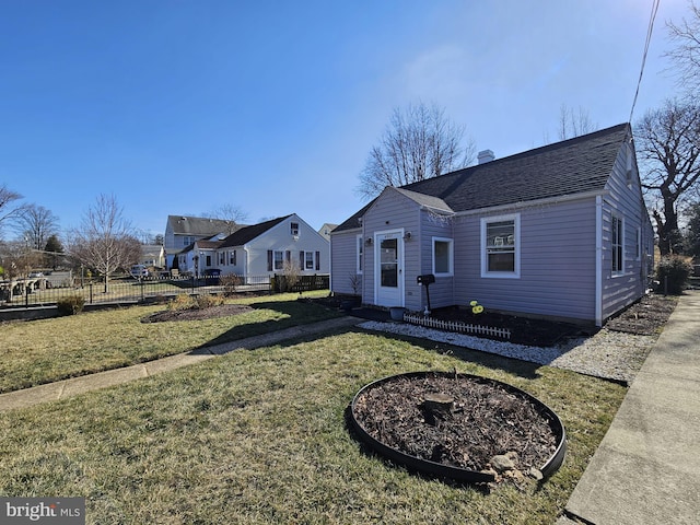 view of front of home with a shingled roof, a chimney, a front yard, and fence