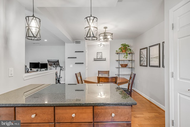 kitchen with dark stone counters, brown cabinetry, visible vents, and light wood-style floors