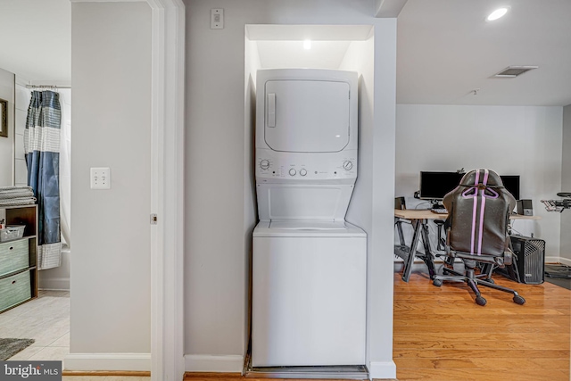 laundry area with laundry area, visible vents, baseboards, light wood-type flooring, and stacked washing maching and dryer