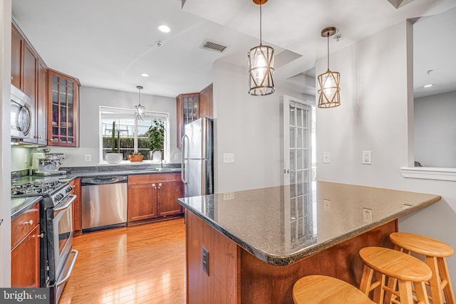 kitchen featuring visible vents, light wood-style floors, appliances with stainless steel finishes, a kitchen bar, and glass insert cabinets