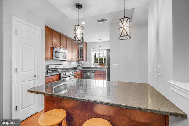 kitchen with a breakfast bar, stainless steel appliances, visible vents, glass insert cabinets, and dark stone countertops