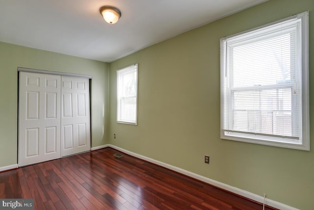 unfurnished bedroom featuring multiple windows, a closet, and dark hardwood / wood-style floors