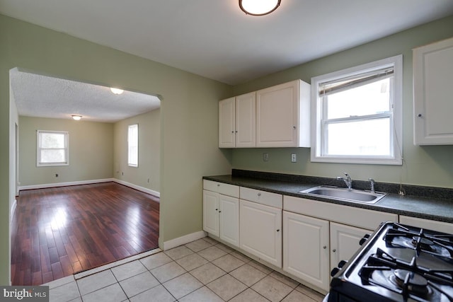 kitchen with black range with gas stovetop, sink, white cabinets, and a textured ceiling