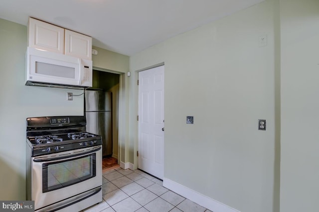 kitchen with fridge, white cabinets, light tile patterned floors, and stainless steel gas range oven