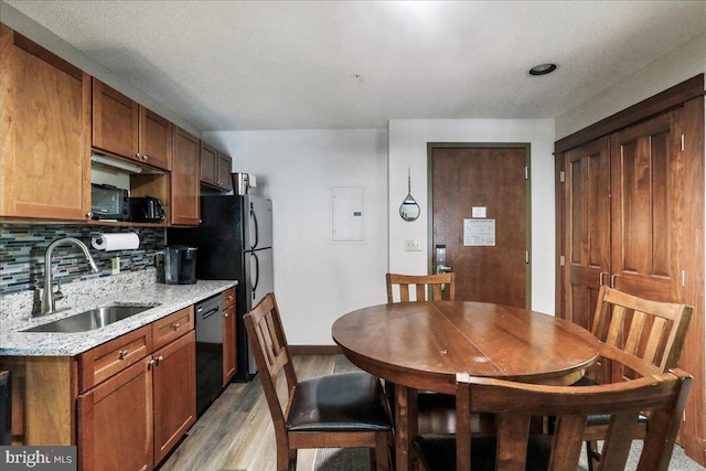 kitchen featuring sink, black dishwasher, light stone countertops, light hardwood / wood-style floors, and backsplash