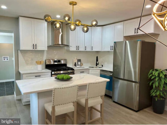 kitchen with wall chimney exhaust hood, sink, decorative light fixtures, appliances with stainless steel finishes, and white cabinets