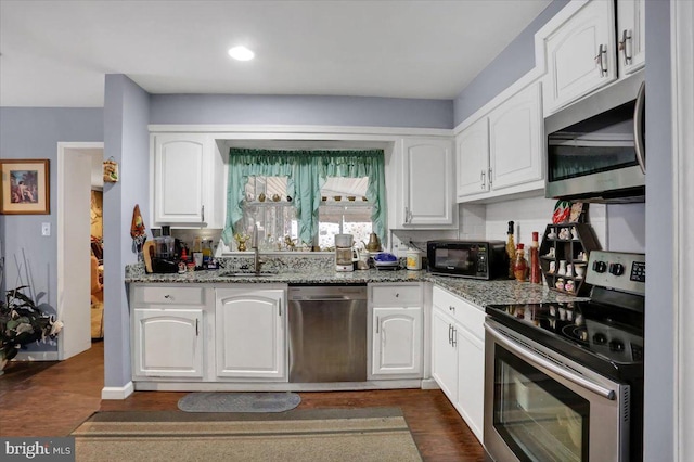 kitchen featuring stone counters, a sink, white cabinets, appliances with stainless steel finishes, and dark wood finished floors