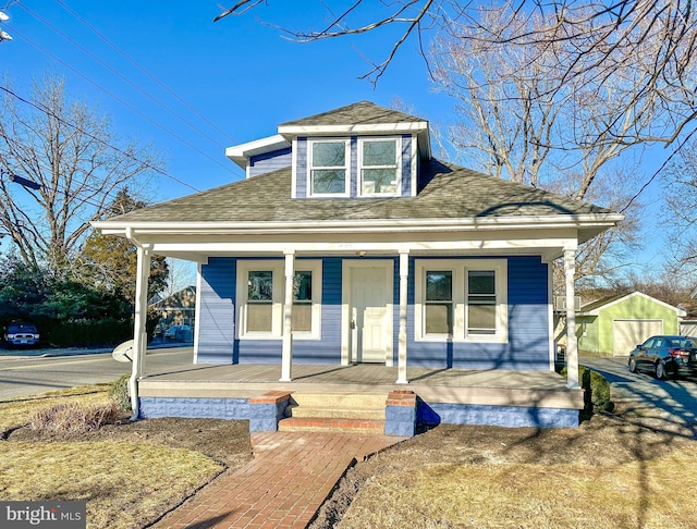 bungalow-style house featuring covered porch, a shed, a shingled roof, and an outbuilding