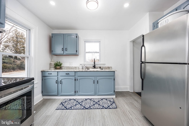 kitchen with stainless steel appliances, light wood-type flooring, a sink, and blue cabinetry