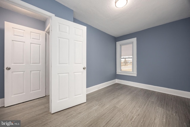 unfurnished bedroom featuring light wood-style floors, a textured ceiling, and baseboards