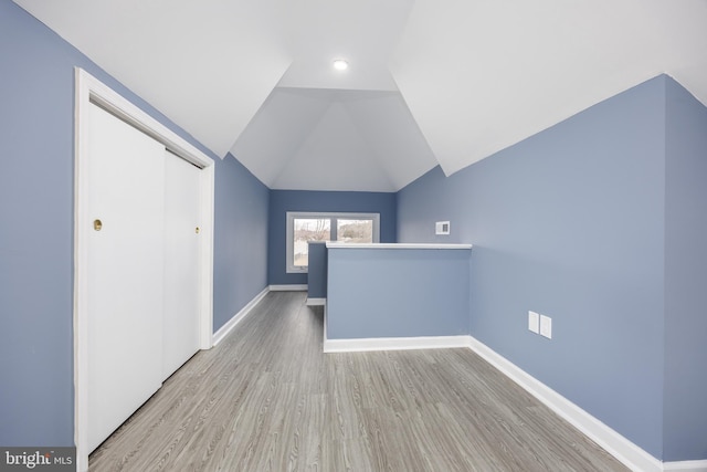 additional living space featuring vaulted ceiling, light wood-style flooring, and baseboards