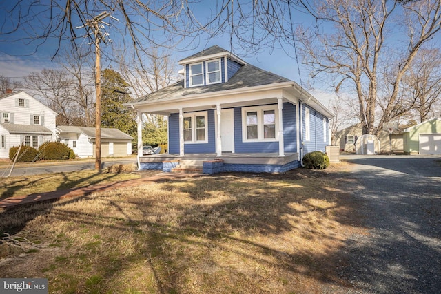 bungalow with a porch, a front yard, and an outdoor structure