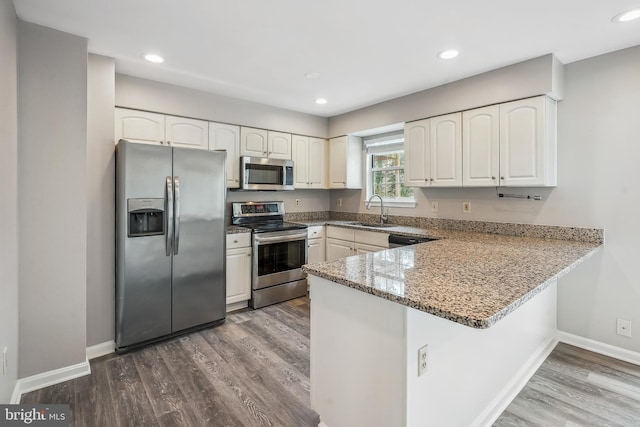 kitchen with a peninsula, white cabinets, dark wood-type flooring, and stainless steel appliances