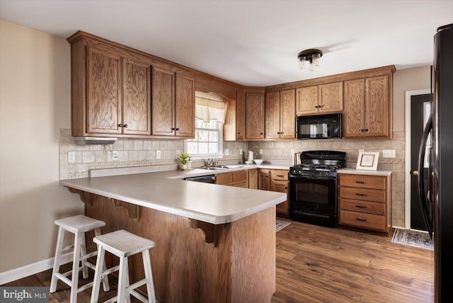 kitchen featuring tasteful backsplash, black appliances, sink, a kitchen bar, and kitchen peninsula