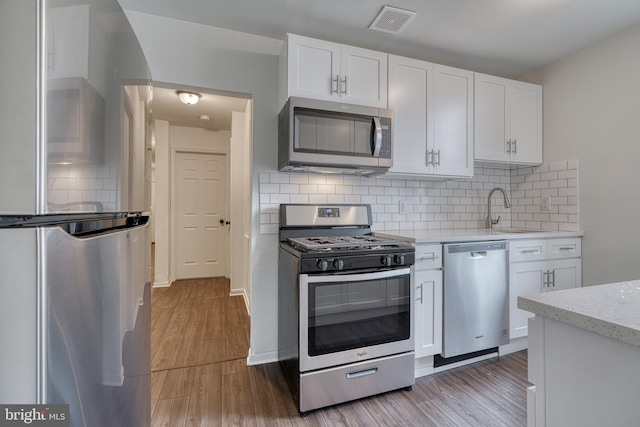 kitchen featuring a sink, visible vents, white cabinets, light wood-style floors, and appliances with stainless steel finishes