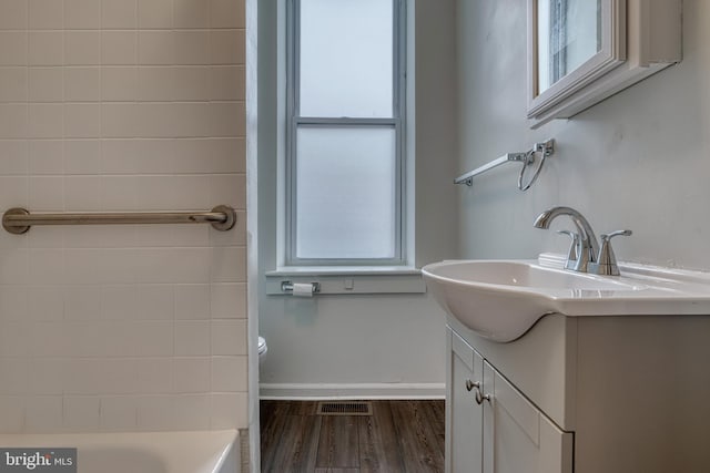 full bath with visible vents, a bathing tub, vanity, wood finished floors, and baseboards