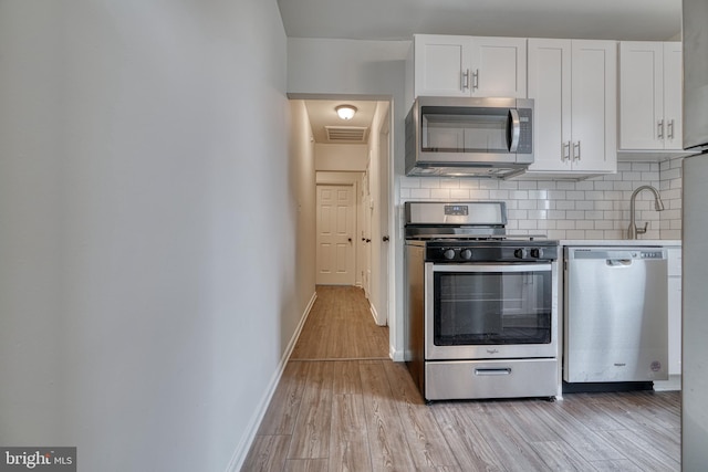 kitchen with visible vents, white cabinets, appliances with stainless steel finishes, light wood-type flooring, and backsplash