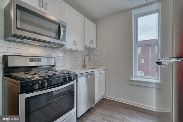 kitchen featuring stainless steel appliances, a sink, white cabinetry, light countertops, and backsplash