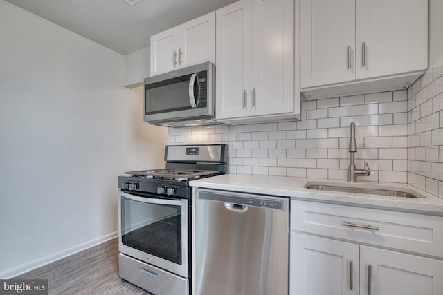 kitchen featuring light wood-style flooring, decorative backsplash, appliances with stainless steel finishes, white cabinets, and a sink