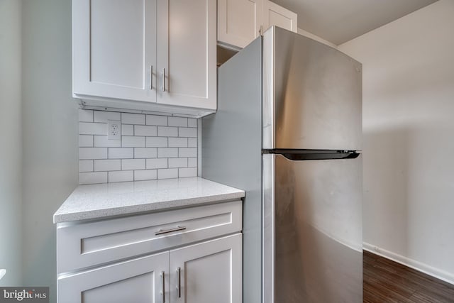 kitchen featuring light stone counters, baseboards, freestanding refrigerator, tasteful backsplash, and dark wood finished floors