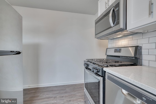 kitchen featuring stainless steel appliances, tasteful backsplash, light wood-style flooring, white cabinetry, and baseboards