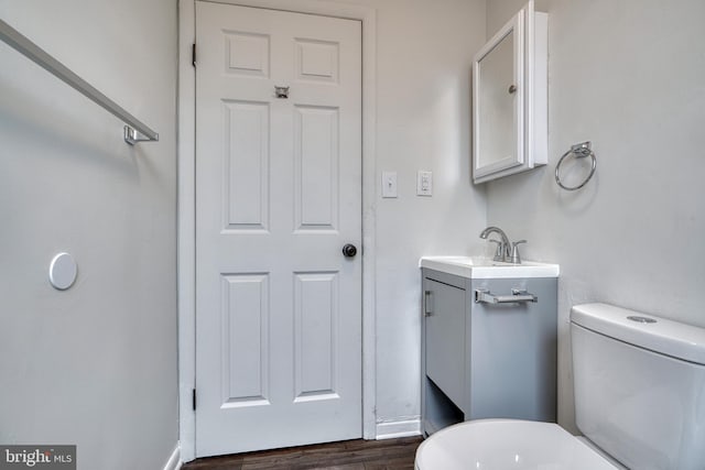 half bath featuring wood finished floors, vanity, toilet, and baseboards