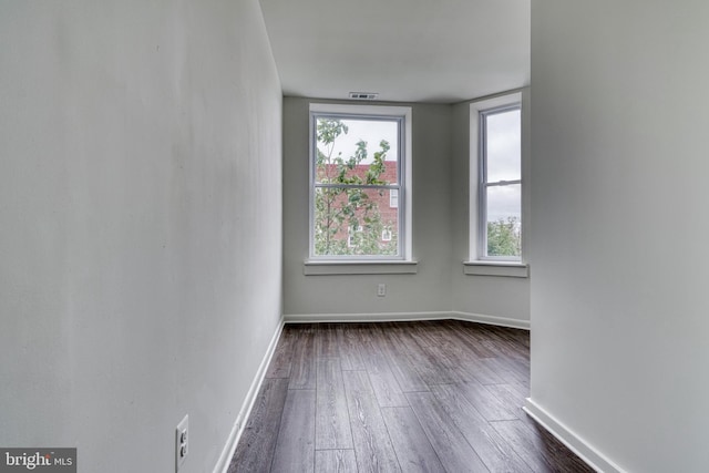 spare room with dark wood-style flooring, visible vents, and baseboards