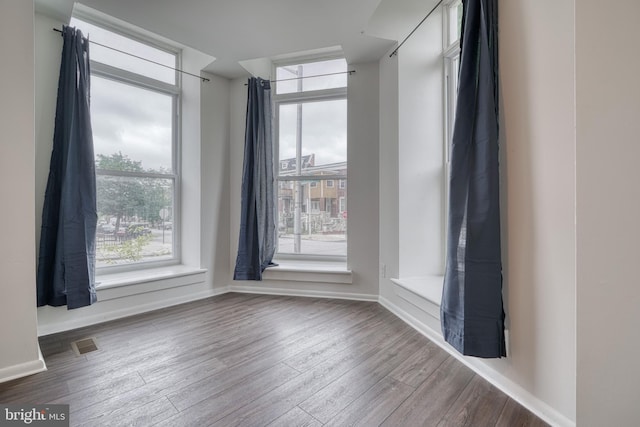 spare room with wood finished floors, visible vents, and baseboards