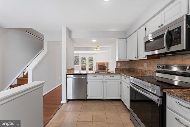 kitchen featuring stainless steel appliances, backsplash, white cabinetry, a sink, and dark stone counters