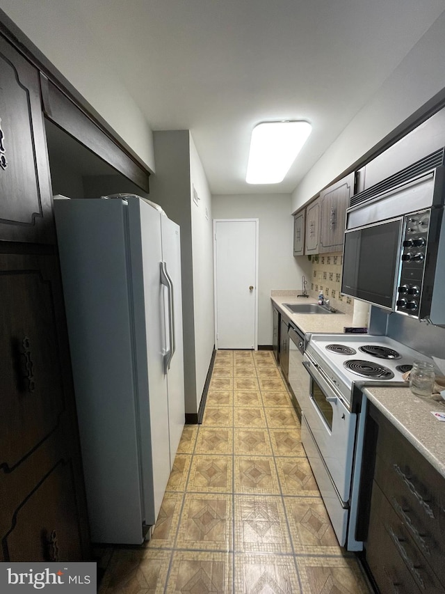 kitchen featuring light countertops, appliances with stainless steel finishes, a sink, dark brown cabinetry, and baseboards