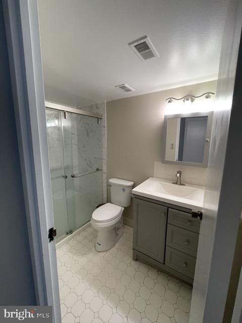 bathroom with toilet, vanity, a shower stall, and visible vents