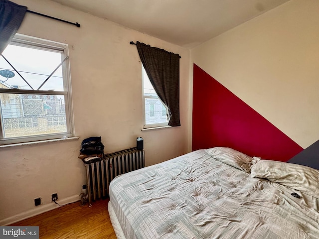 bedroom with wood-type flooring, radiator, and multiple windows