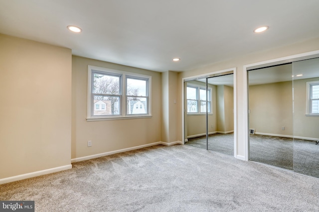 unfurnished bedroom with multiple closets, multiple windows, and light carpet