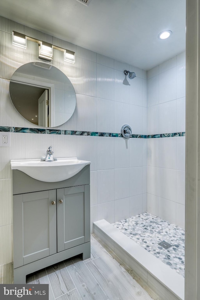 bathroom with vanity, a tile shower, and tile walls