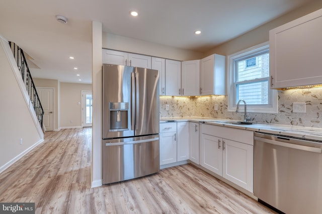 kitchen with appliances with stainless steel finishes, light hardwood / wood-style floors, decorative backsplash, and white cabinets