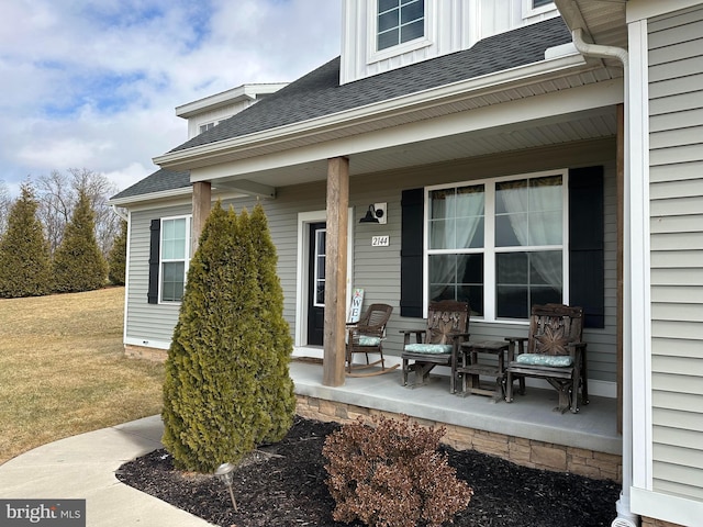 entrance to property featuring a shingled roof, covered porch, and a lawn