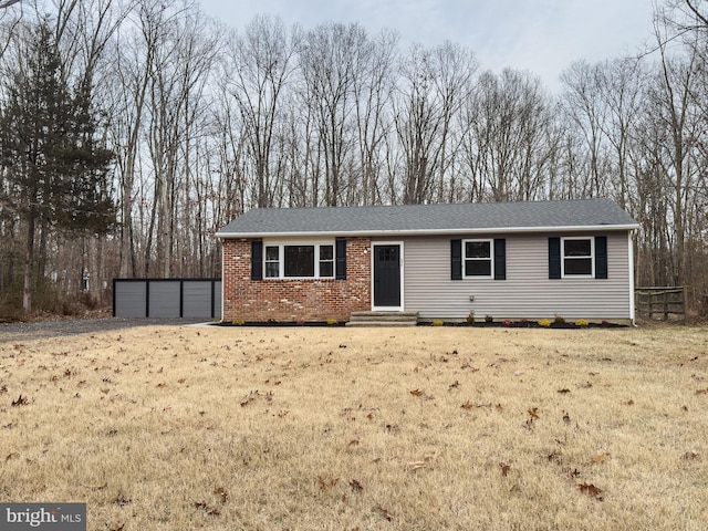 ranch-style house with an outbuilding, brick siding, a shingled roof, a front yard, and a garage