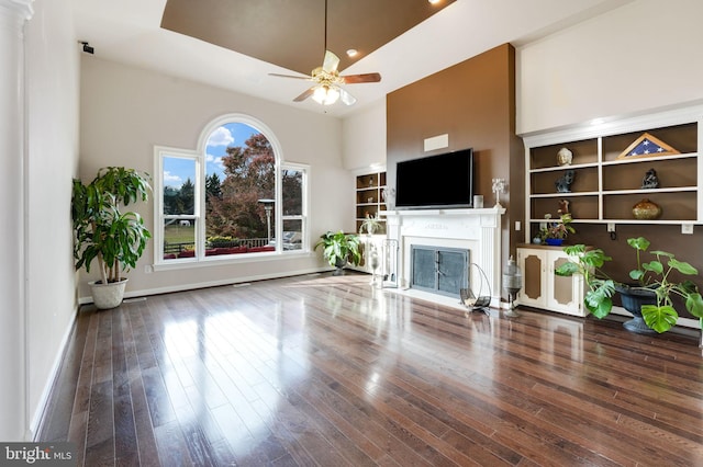 unfurnished living room featuring a ceiling fan, built in features, baseboards, hardwood / wood-style floors, and a glass covered fireplace