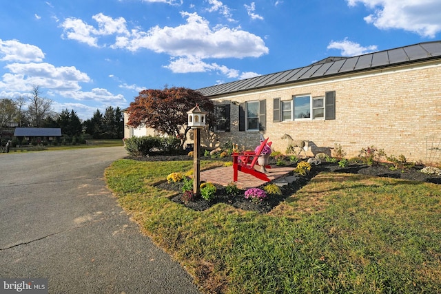 view of side of property featuring metal roof, brick siding, driveway, a lawn, and a standing seam roof