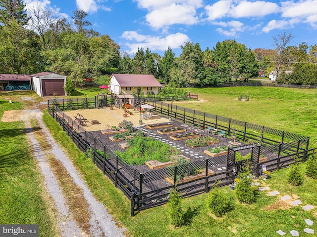 view of yard with driveway, a detached garage, a rural view, fence, and an outdoor structure