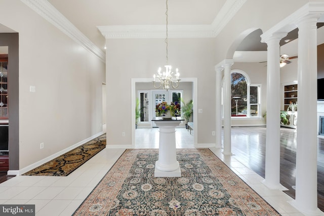 foyer entrance featuring light tile patterned floors, ornate columns, ornamental molding, baseboards, and ceiling fan with notable chandelier