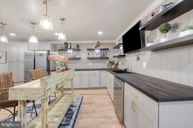 kitchen featuring crown molding, open shelves, appliances with stainless steel finishes, light wood-style floors, and a sink