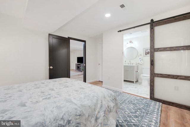 bedroom featuring a barn door, connected bathroom, visible vents, baseboards, and marble finish floor