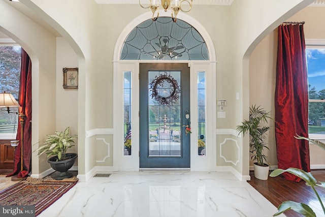 foyer entrance featuring a chandelier, arched walkways, marble finish floor, and baseboards