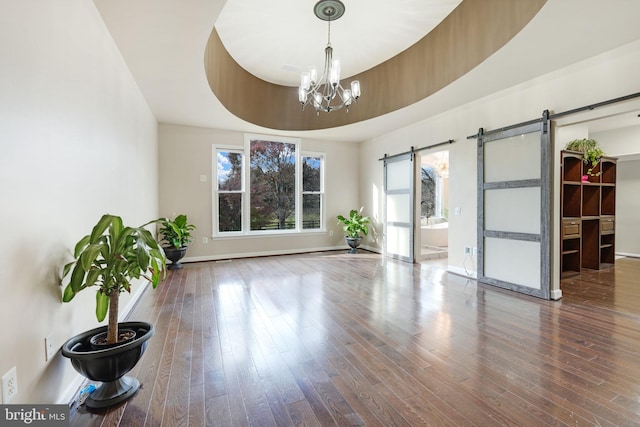 empty room with a barn door, baseboards, wood finished floors, a tray ceiling, and a chandelier