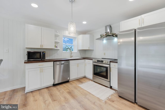 kitchen with stainless steel appliances, a sink, white cabinetry, light wood-style floors, and wall chimney exhaust hood